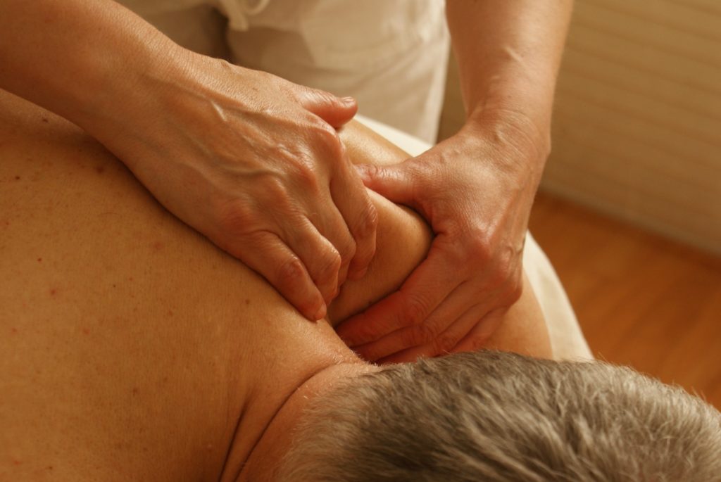 Hands grab a man's shoulder during a massage session.