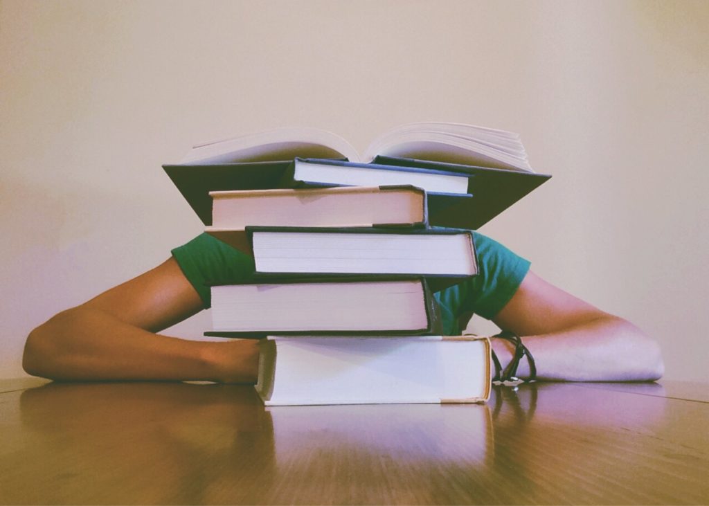 A person is hidden behind a pile of books on a table. Let me teach you about naturopathic medicine instead.