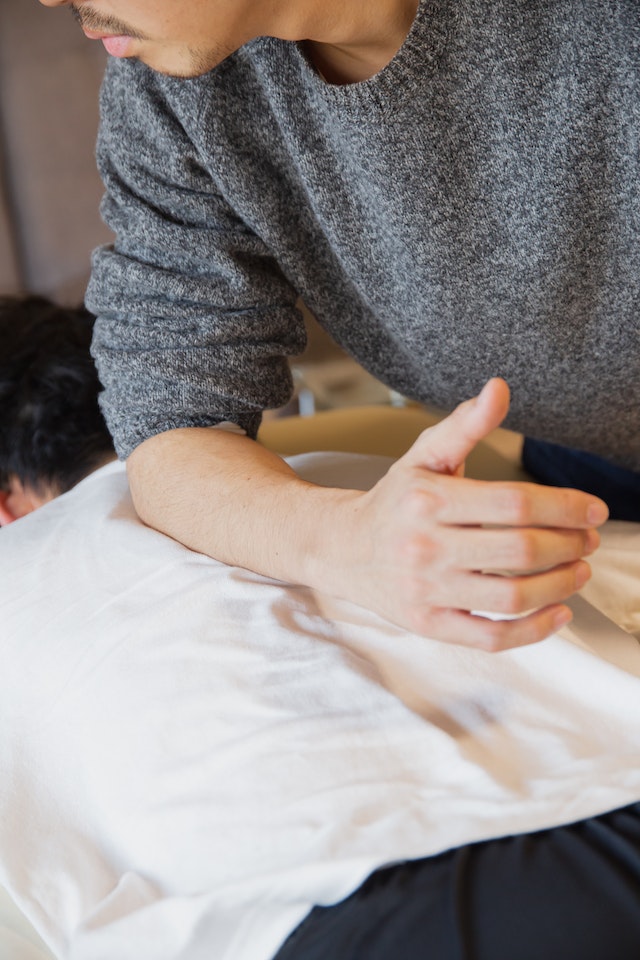 A man places his elbow on a patient's back during a clothed massage.